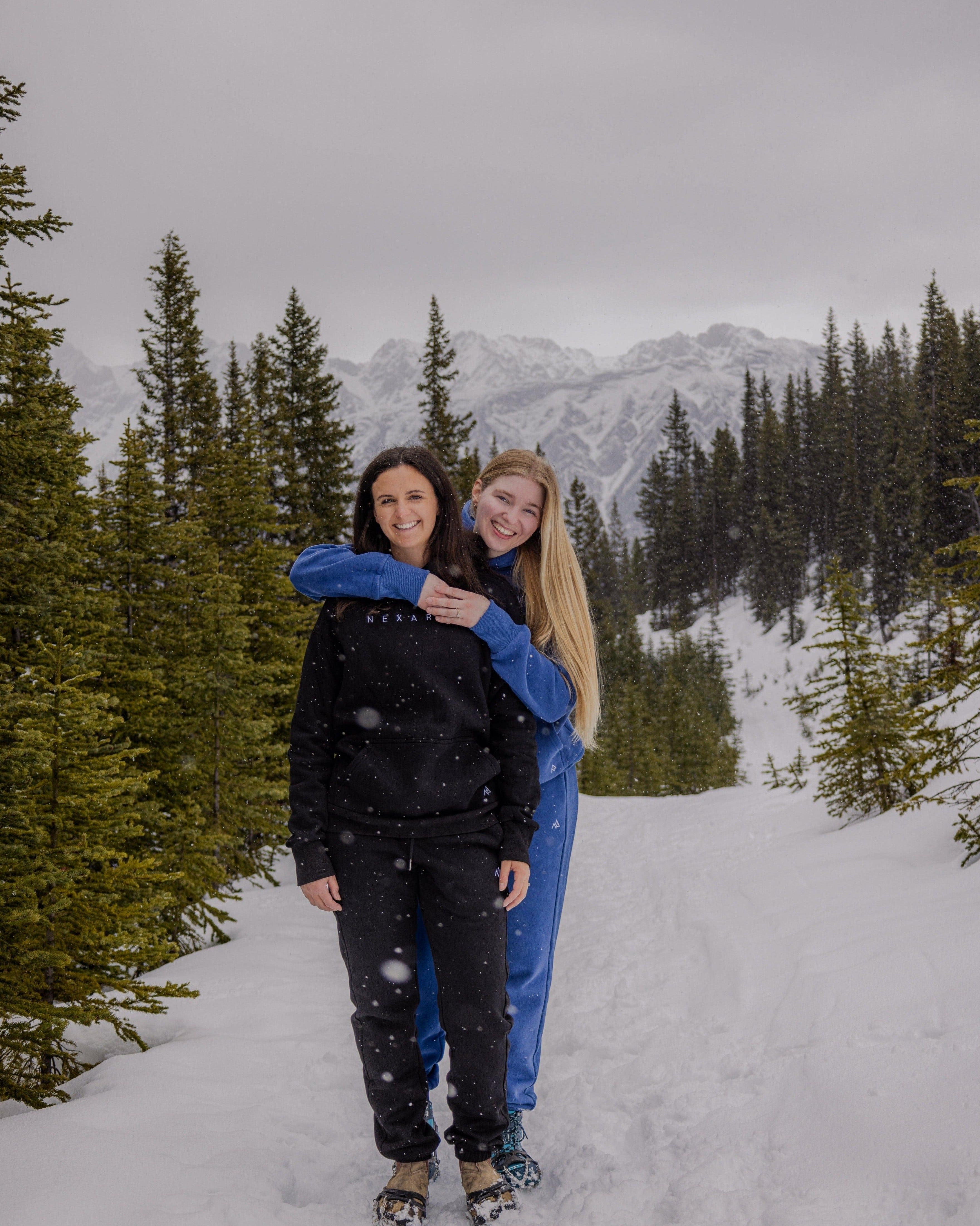 Woman hugging another in Nexarina Blue and Black Sweatsuits outdoors.