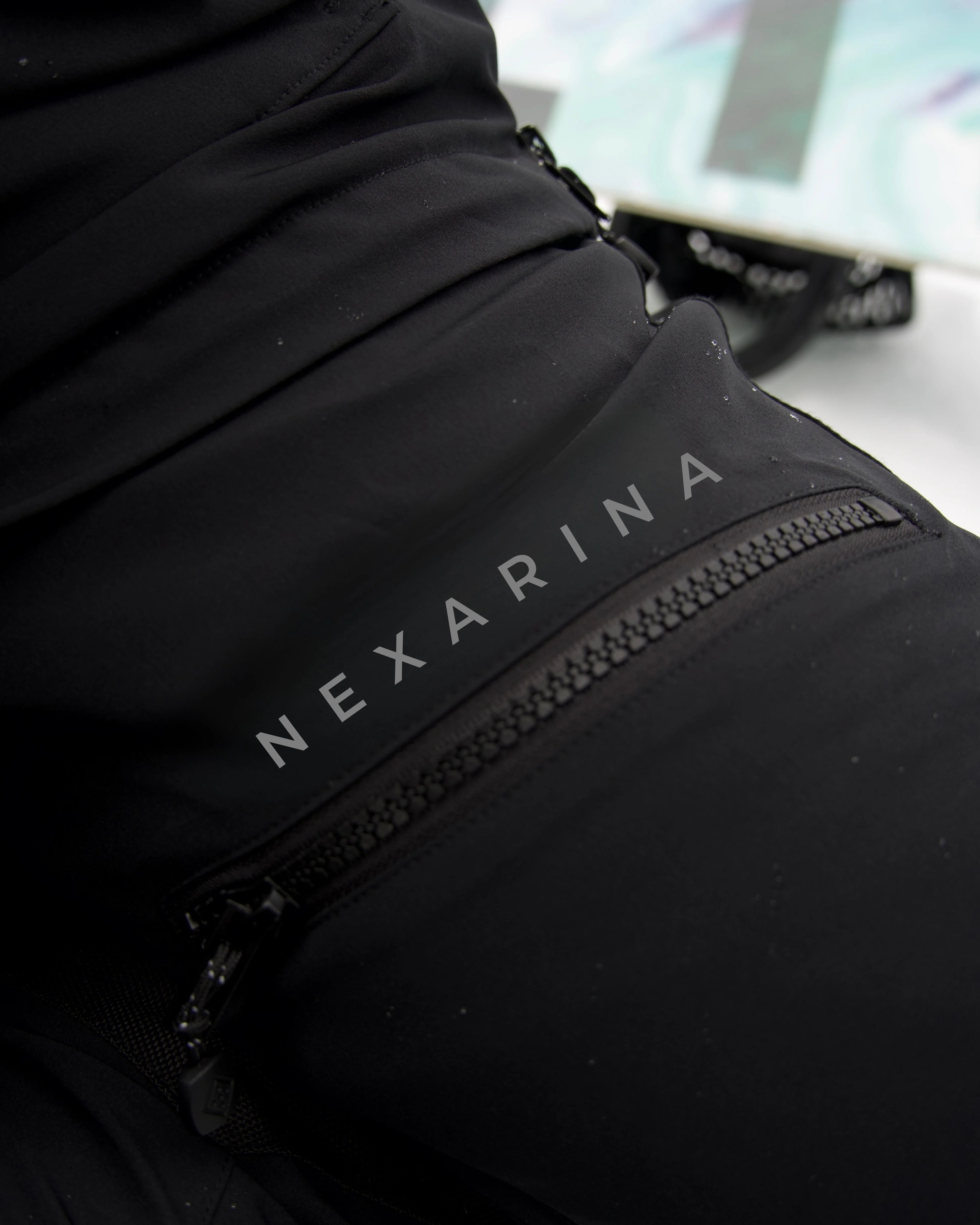 Close-up of Nexarina Avani Snow Pants showing waterproof zipper and printed Nexarina logo.