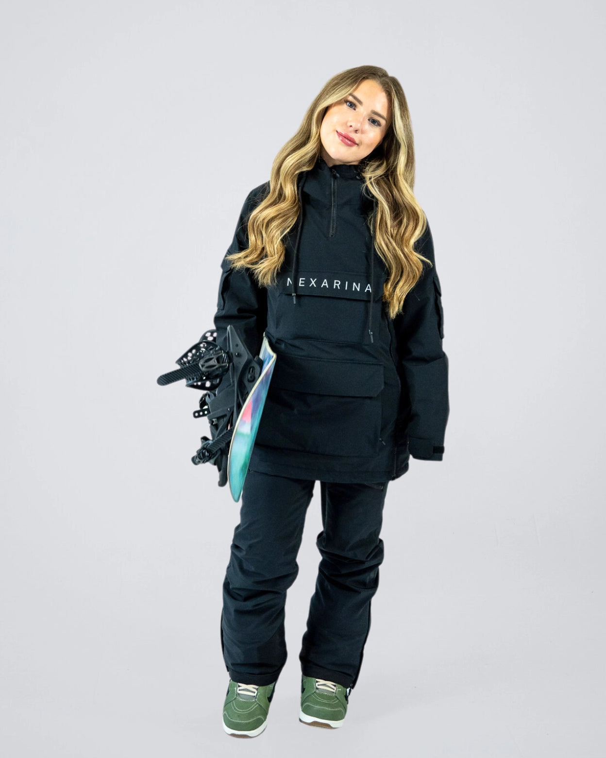 Woman wearing Nexarina Indy black snow jacket holding snowboard, relaxed stance