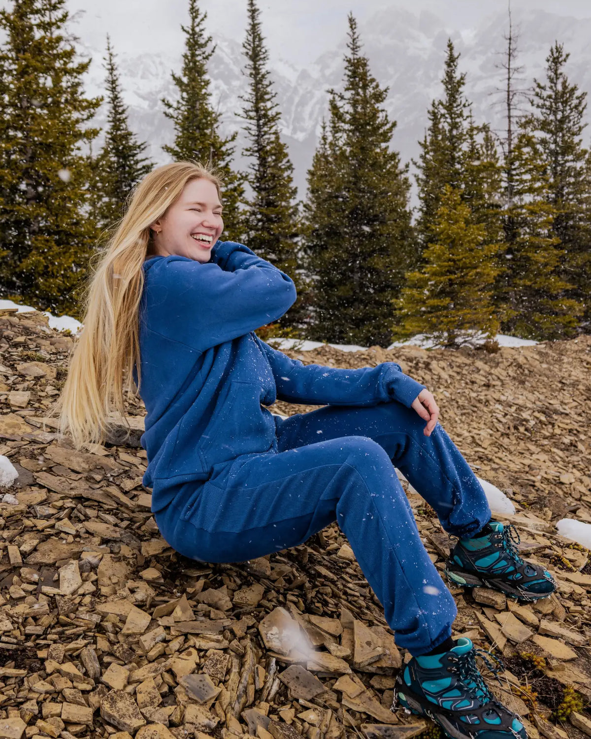 Women's Everly Hoodie in Dusty Blue worn while sitting outdoors in the mountains with matching sweatpants.