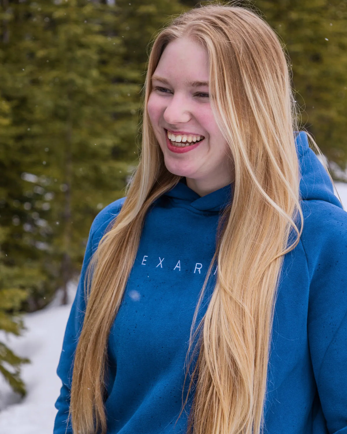Women's Everly Hoodie in Dusty Blue worn outdoors in falling snow with the Nexarina logo visible.