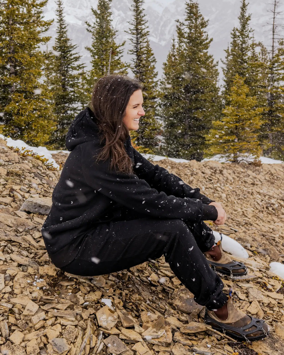 Women's Everly Hoodie in Midnight Black worn with matching sweatpants in a snowy mountain setting.