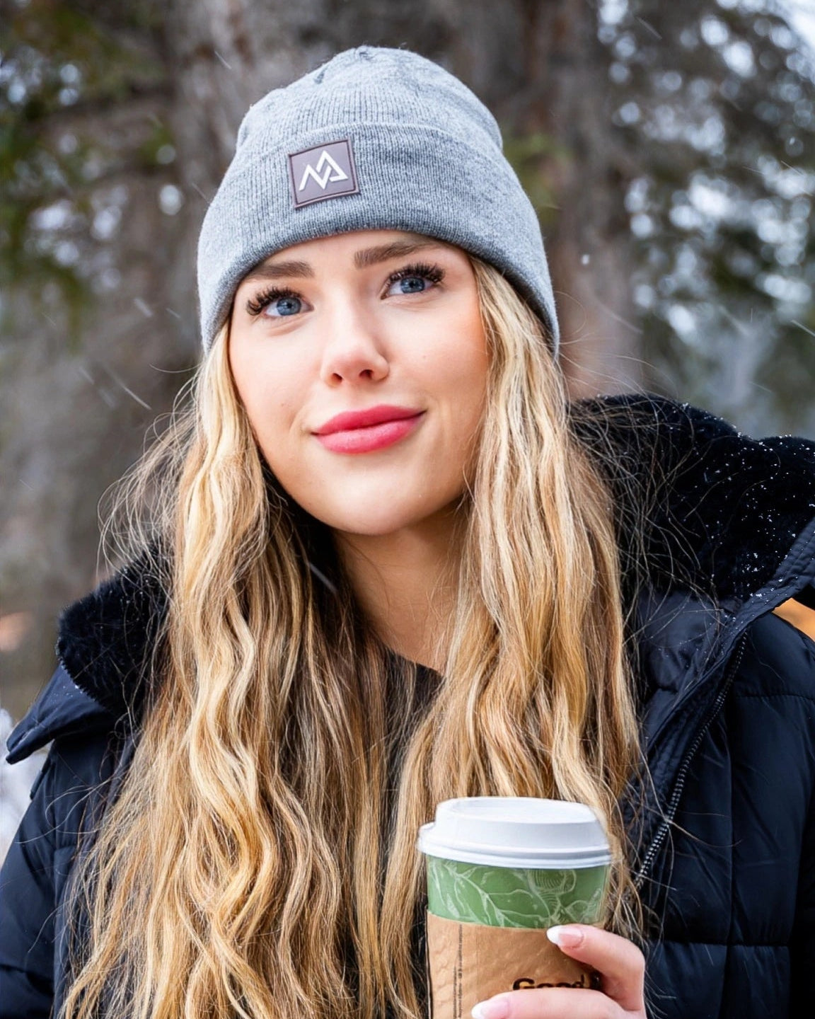 Fashionable winter look featuring a Nexarina Emery Beanie on a woman standing in a snow-covered landscape.