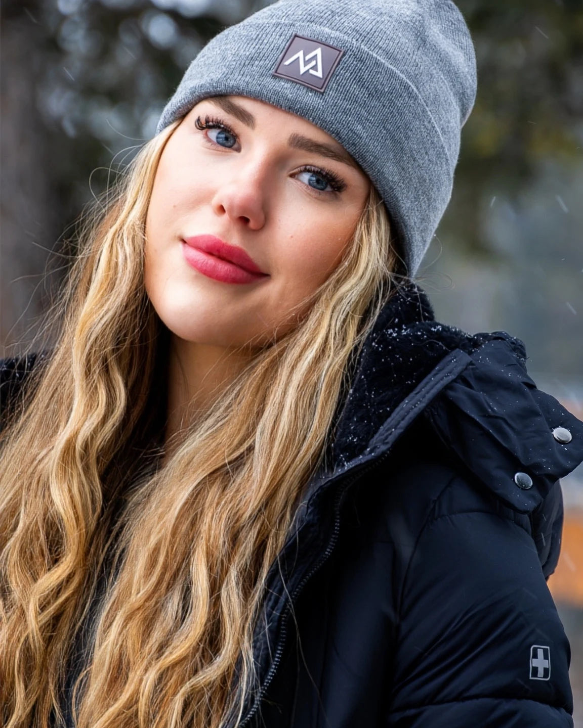 Fashionable winter look featuring a Nexarina Emery Beanie on a woman standing in a snow-covered landscape.