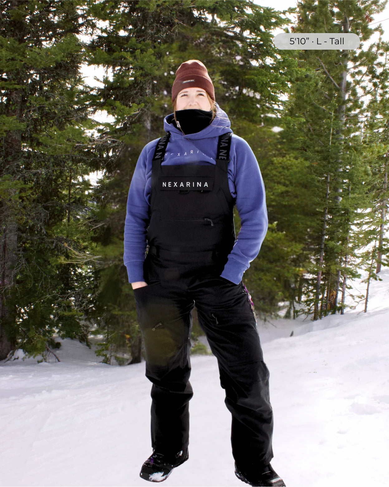 Tall women wearing a blue hoodie and black outerwear bib with 'Nexarina' branding in a snowy forest setting.