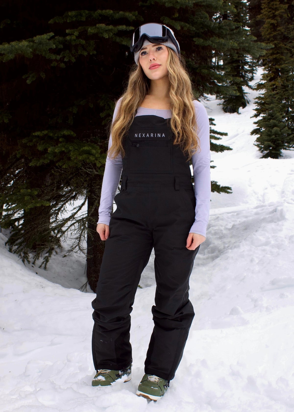 Woman wearing Nexarina Everette Classic Black insulated snow bibs with adjustable shoulder straps in a snowy mountain setting.