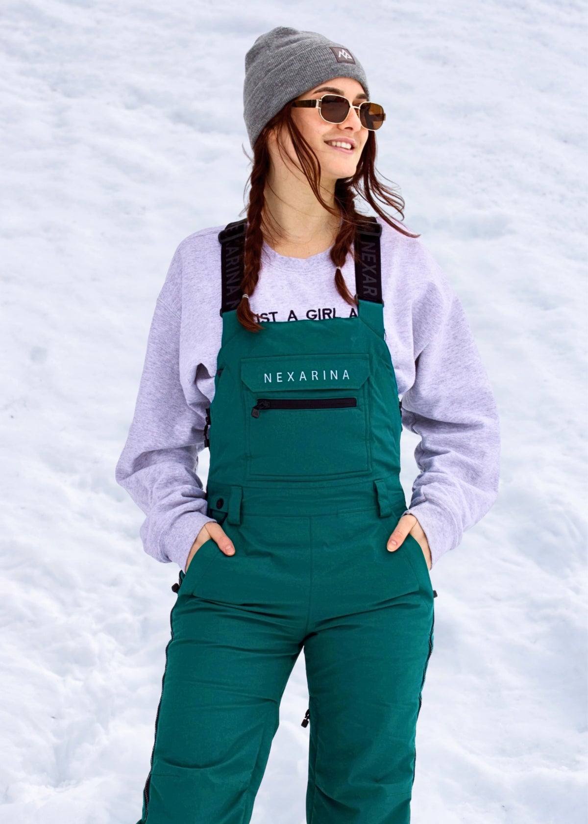 Woman wearing Nexarina Everette Emerald Green insulated snow bibs in a snowy mountain setting.
