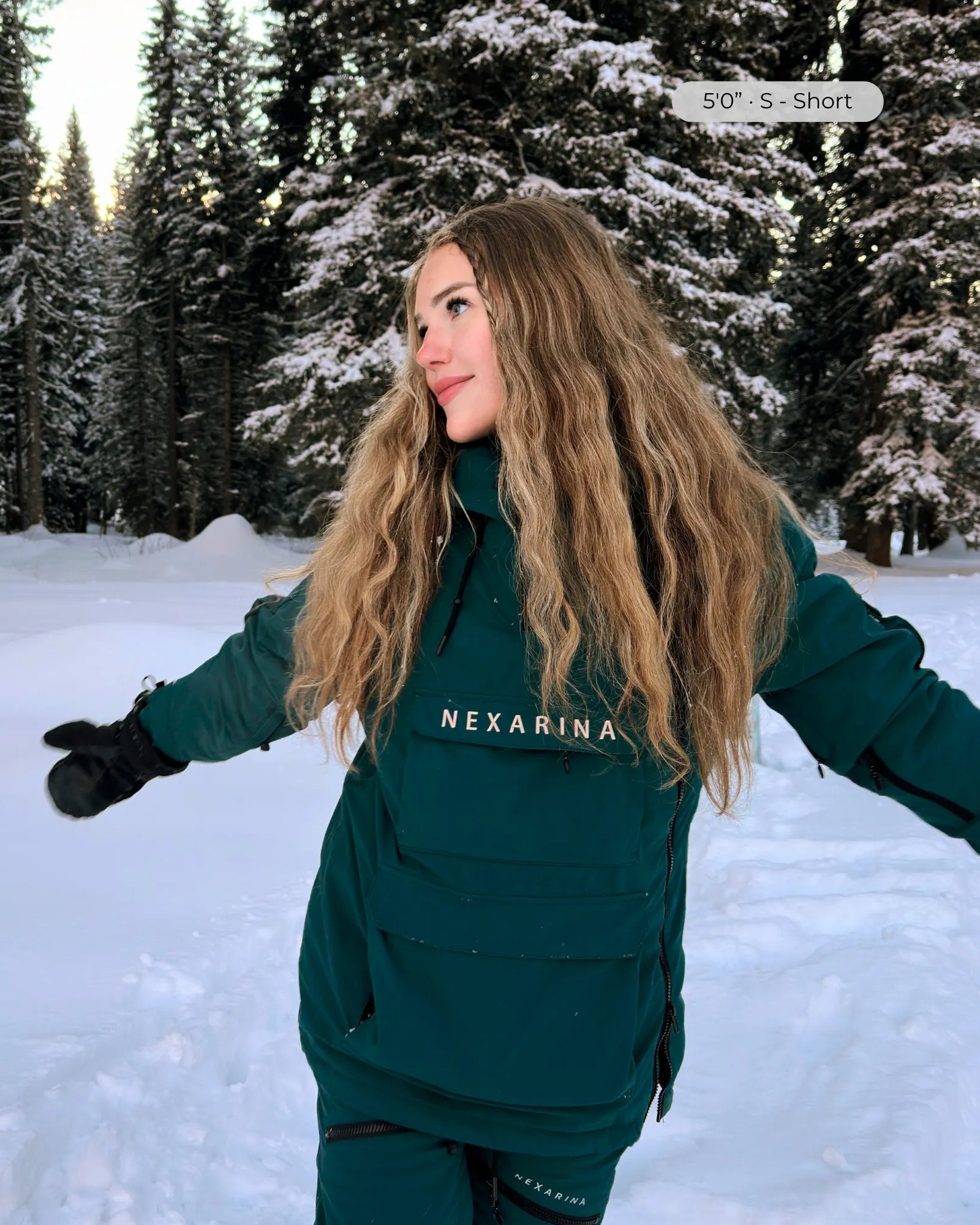 Woman wearing Nexarina Indy emerald green snow jacket, arms out in snowy forest