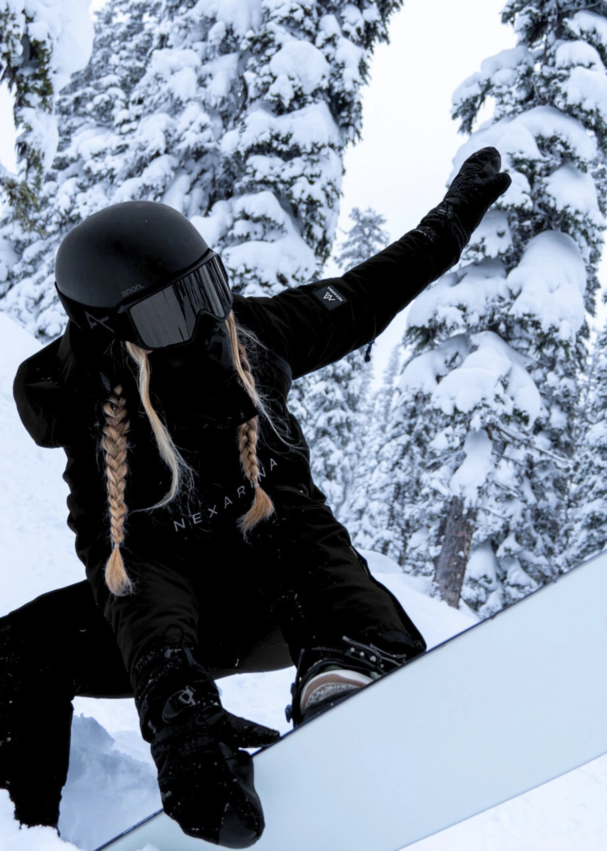 Person snowboarding in a snowy forest wearing black snow gear and helmet.
