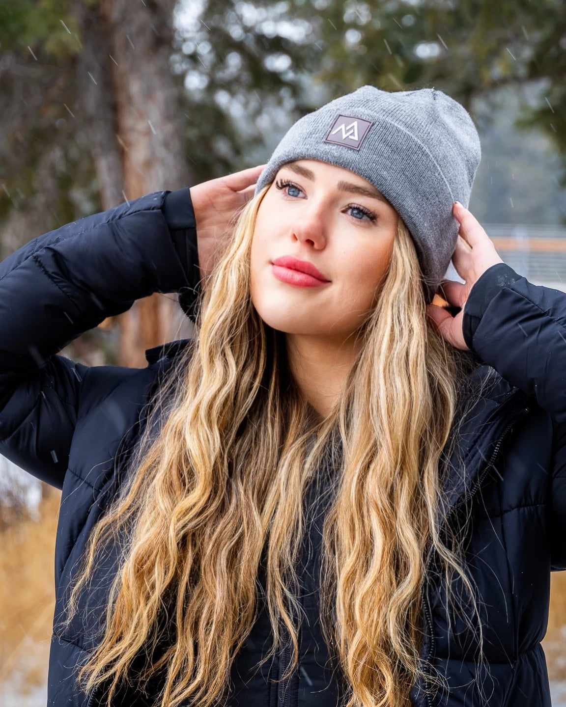 Profile view of a young woman in a grey beanie by Nexarina, gazing into the distance, amidst falling snow.