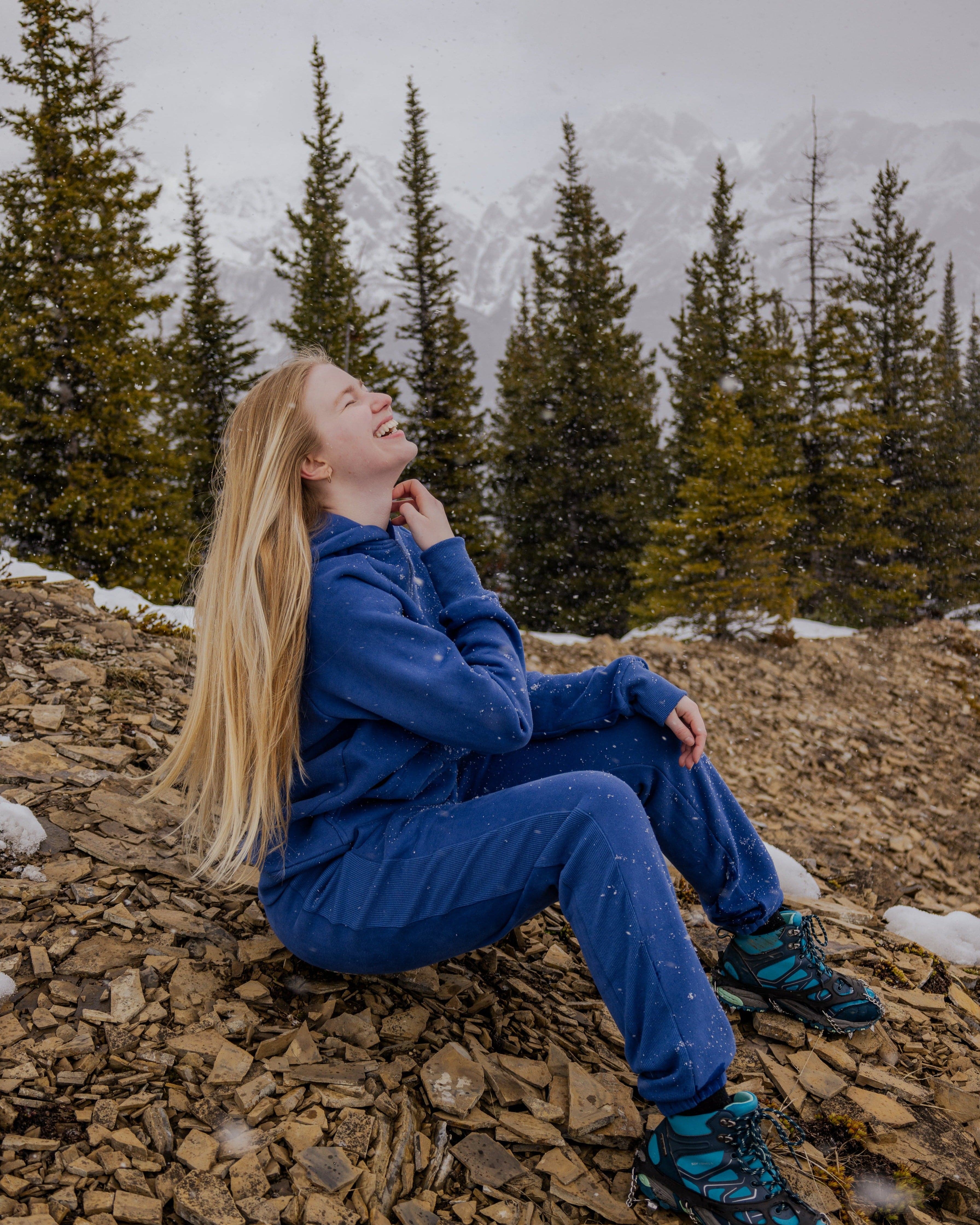 Woman in Nexarina Hoodie laughing while sitting on a snowy mountain.