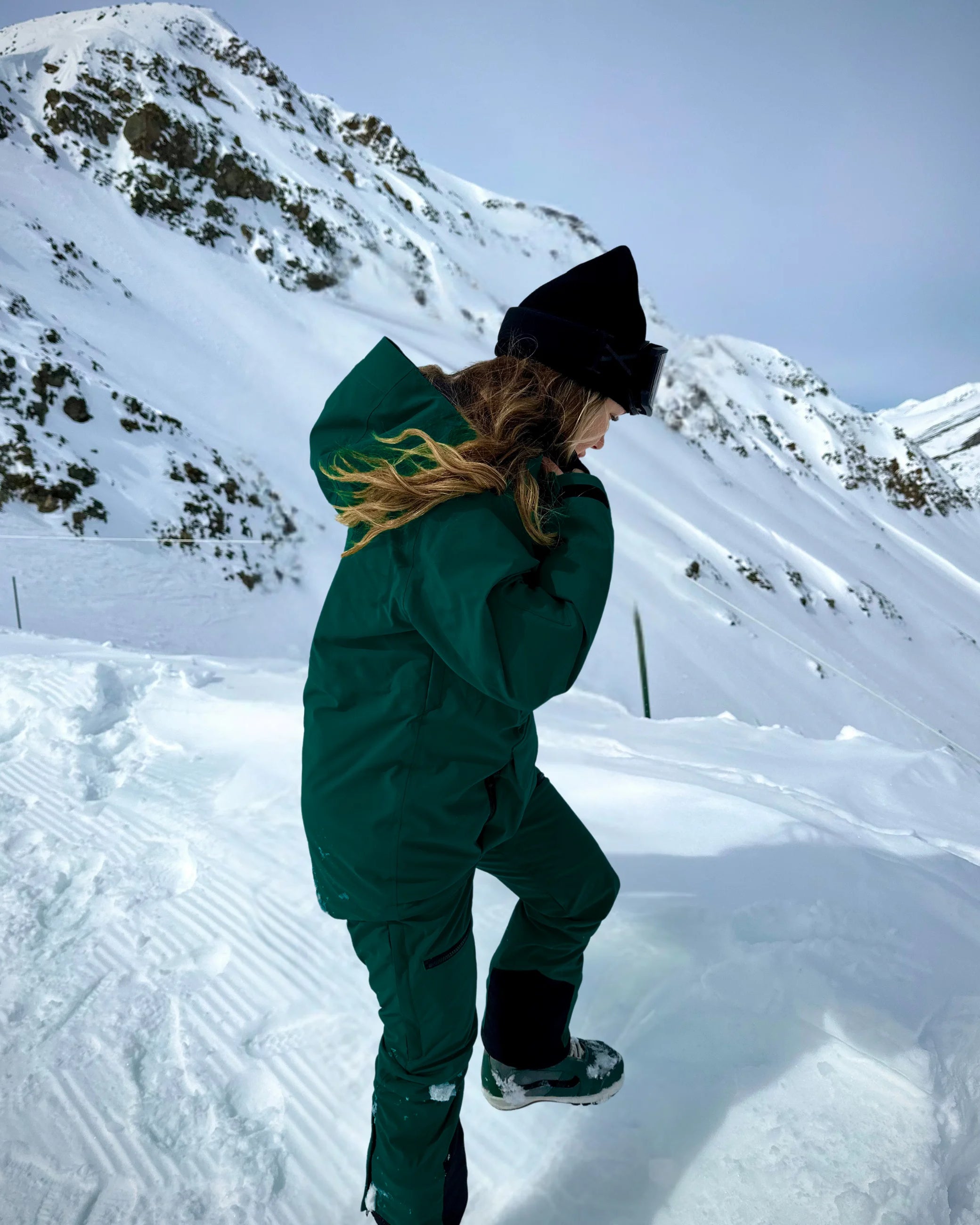 Woman wearing Nexarina Avani snowpants in emerald green with mountain backdrop.