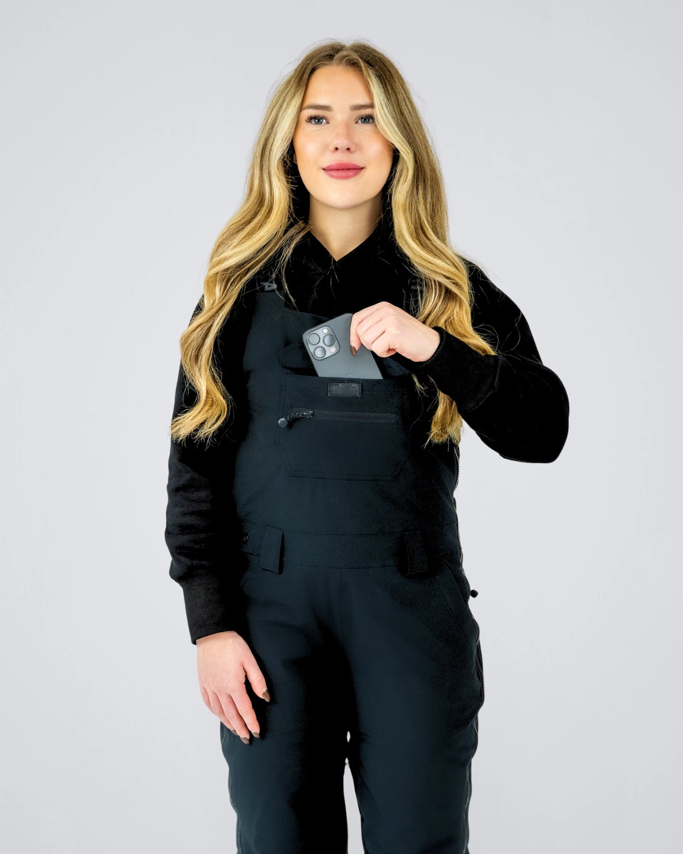 Front view of Nexarina Everette women’s bib snow pants in black, showing chest pocket storage and women’s performance fit.