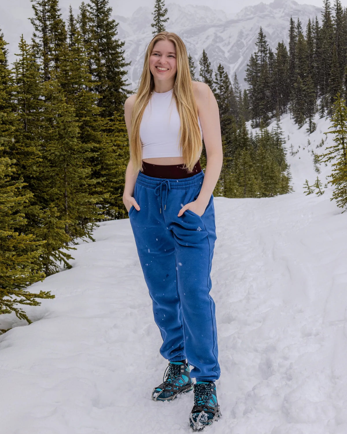 Women's Willow Sweatpants in Dusty Blue worn outdoors in the snow with a mountain backdrop.