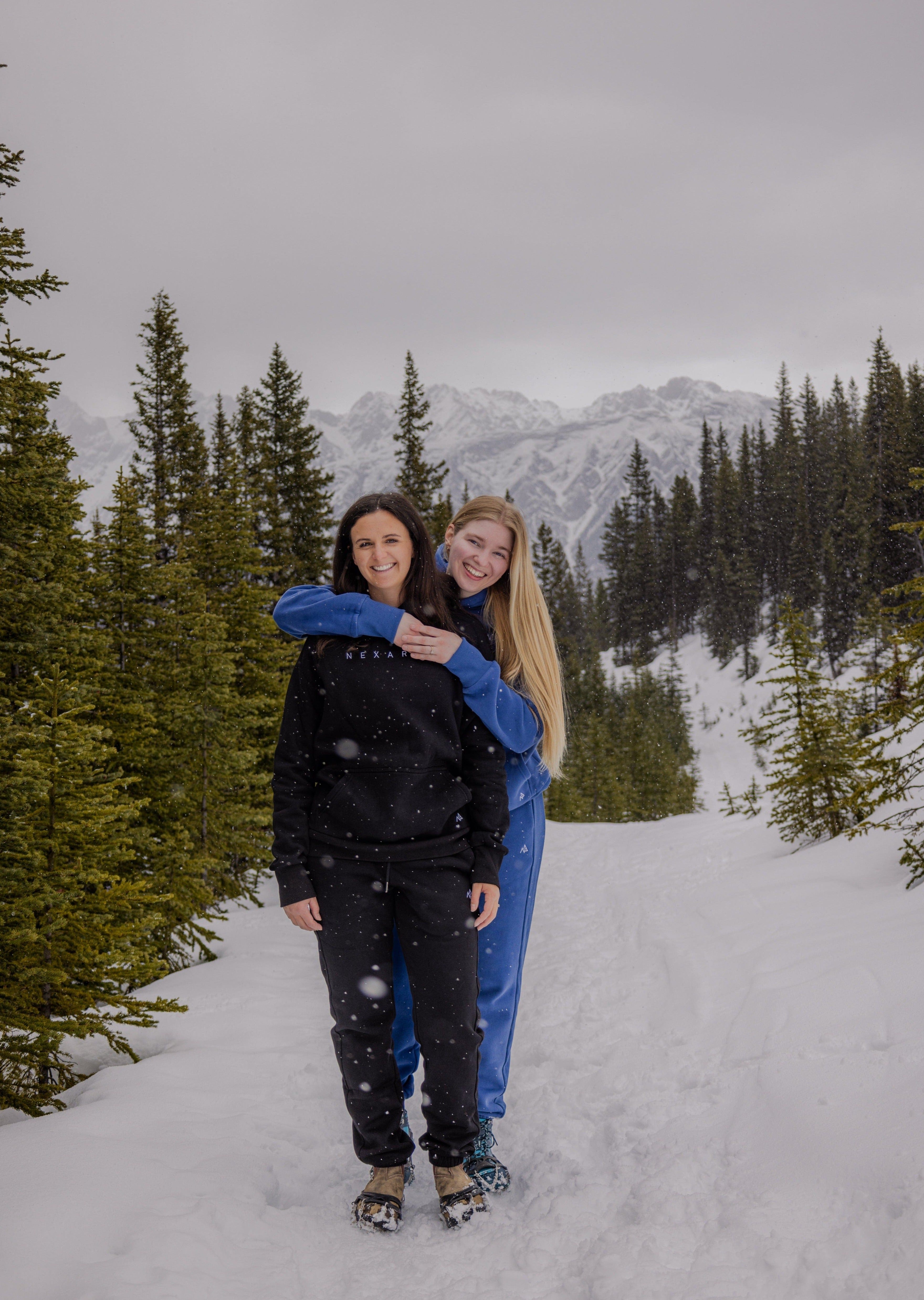 Woman hugging another in Nexarina Blue and Black Sweatsuits outdoors.