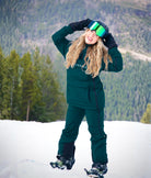 Woman wearing Nexarina emerald green snow jacket and bib pants, full-body view on the mountain.