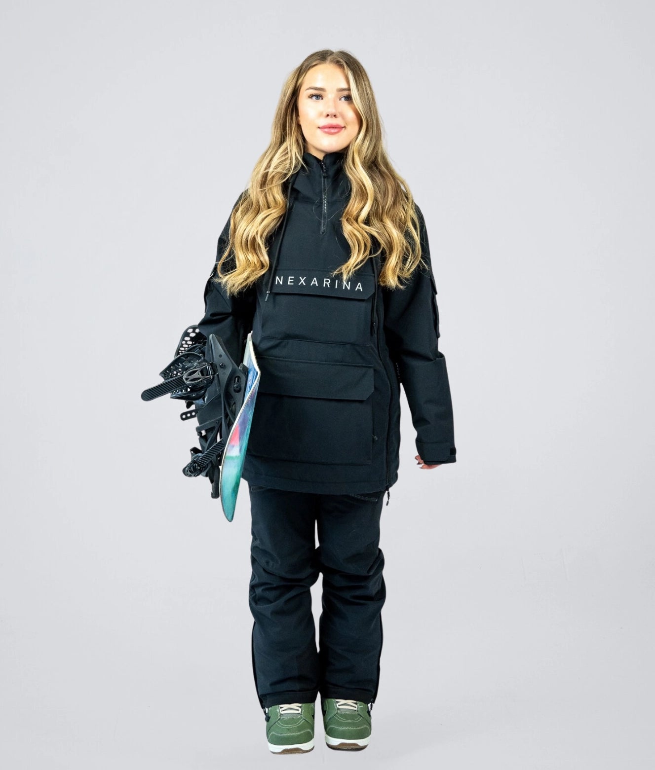 Woman wearing Nexarina Indy snowboarding jacket in black, front view with snowboard