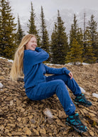 Women's Everly Hoodie in Dusty Blue worn while sitting outdoors in the mountains with matching sweatpants.