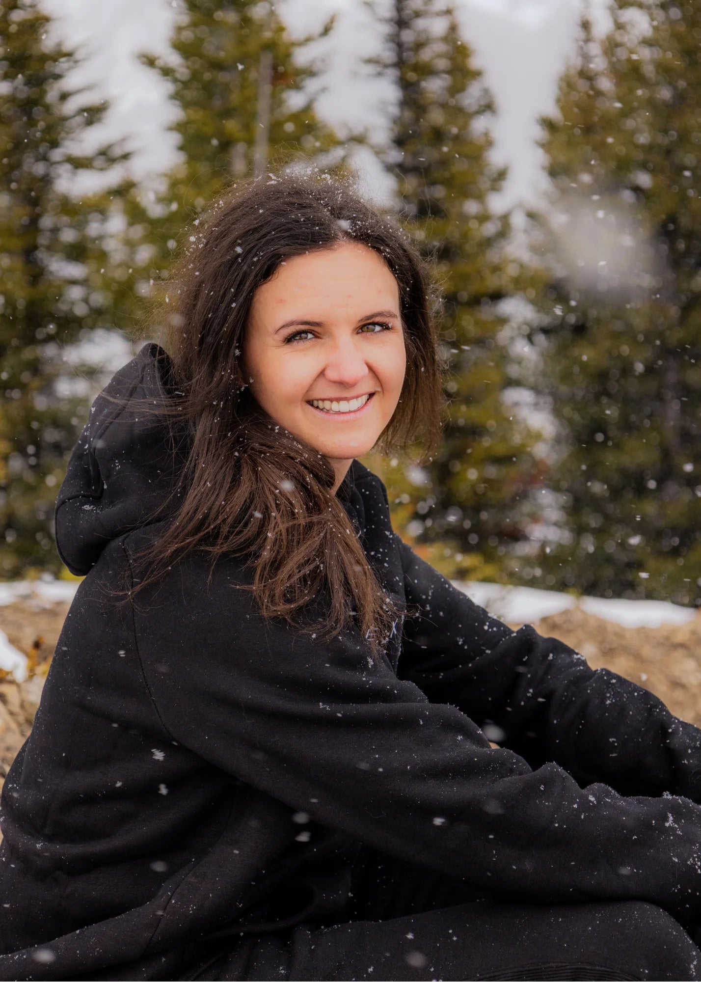 Women's Everly Hoodie in Midnight Black worn outdoors in falling snow.