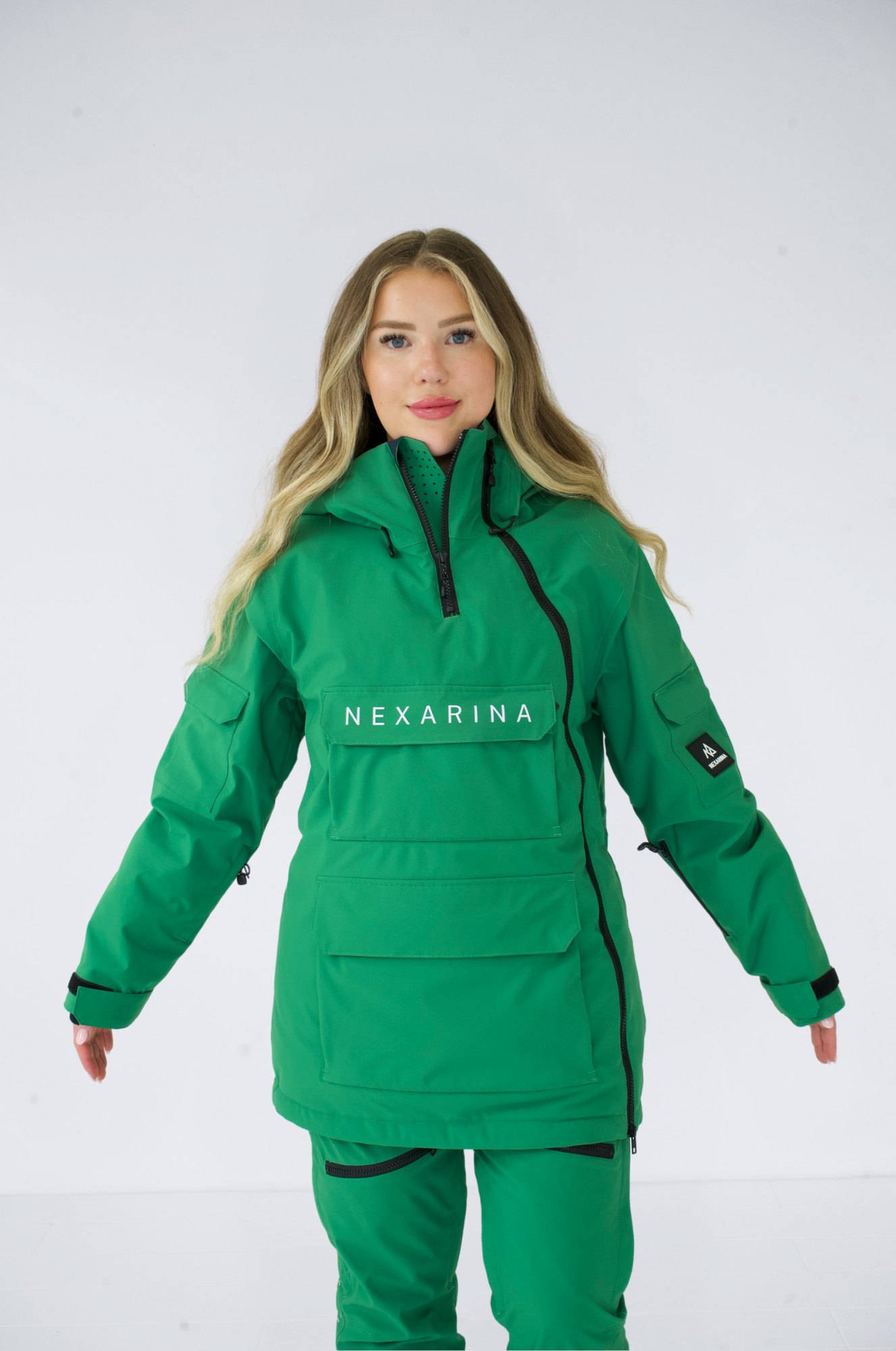 Woman wearing a green Nexarina Indy snow jacket, front view with arms outstretched.