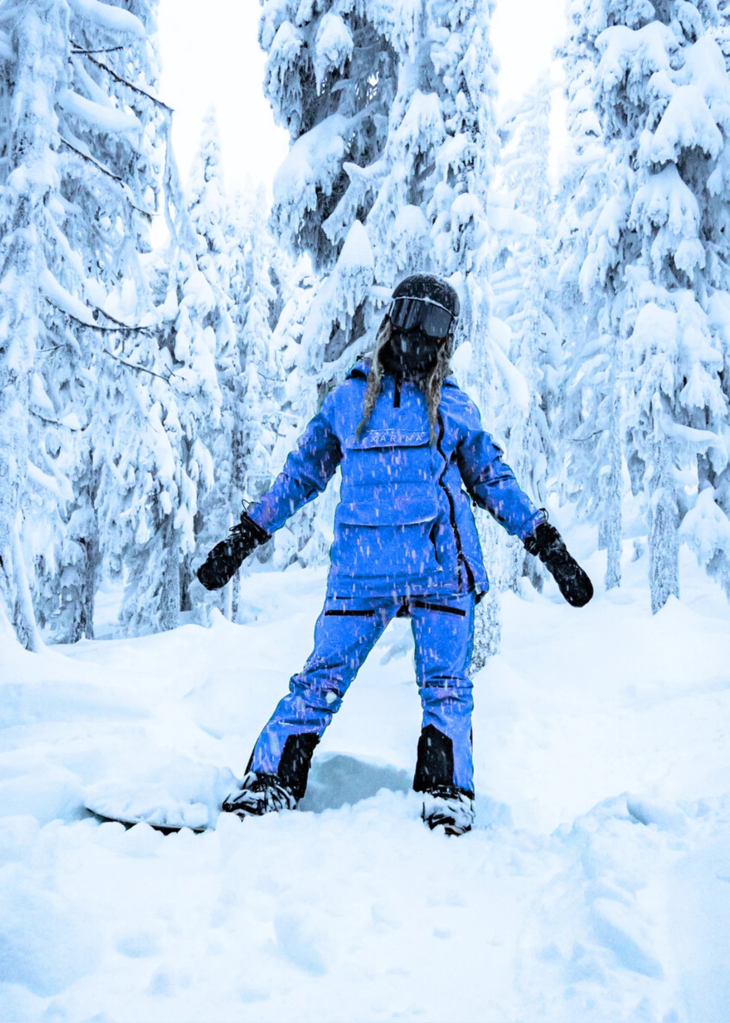 Person in a blue snowsuit standing in a snowy forest