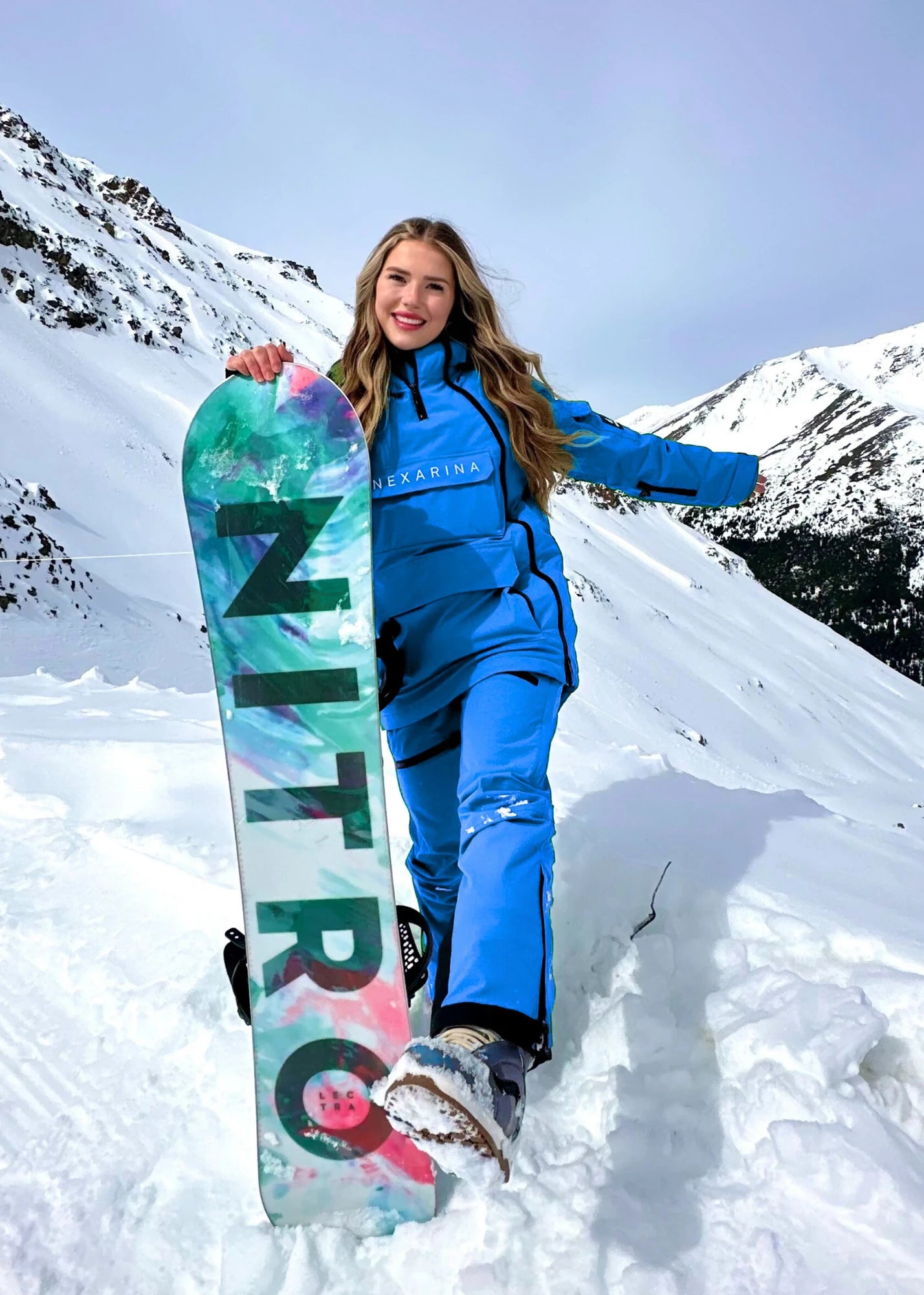 Nexarina Avani women's arctic blue snowboard pants holding Nitro snowboard