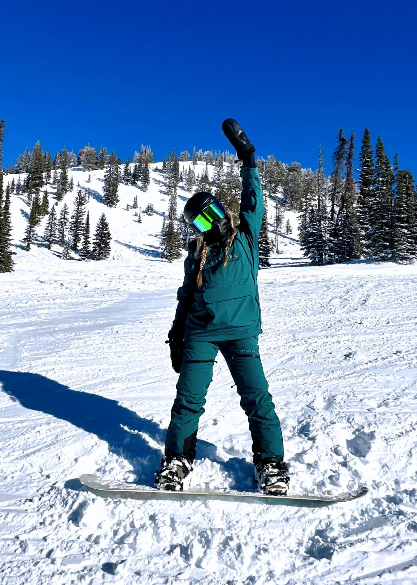 Person snowboarding on a snowy slope with trees and clear blue sky in the background