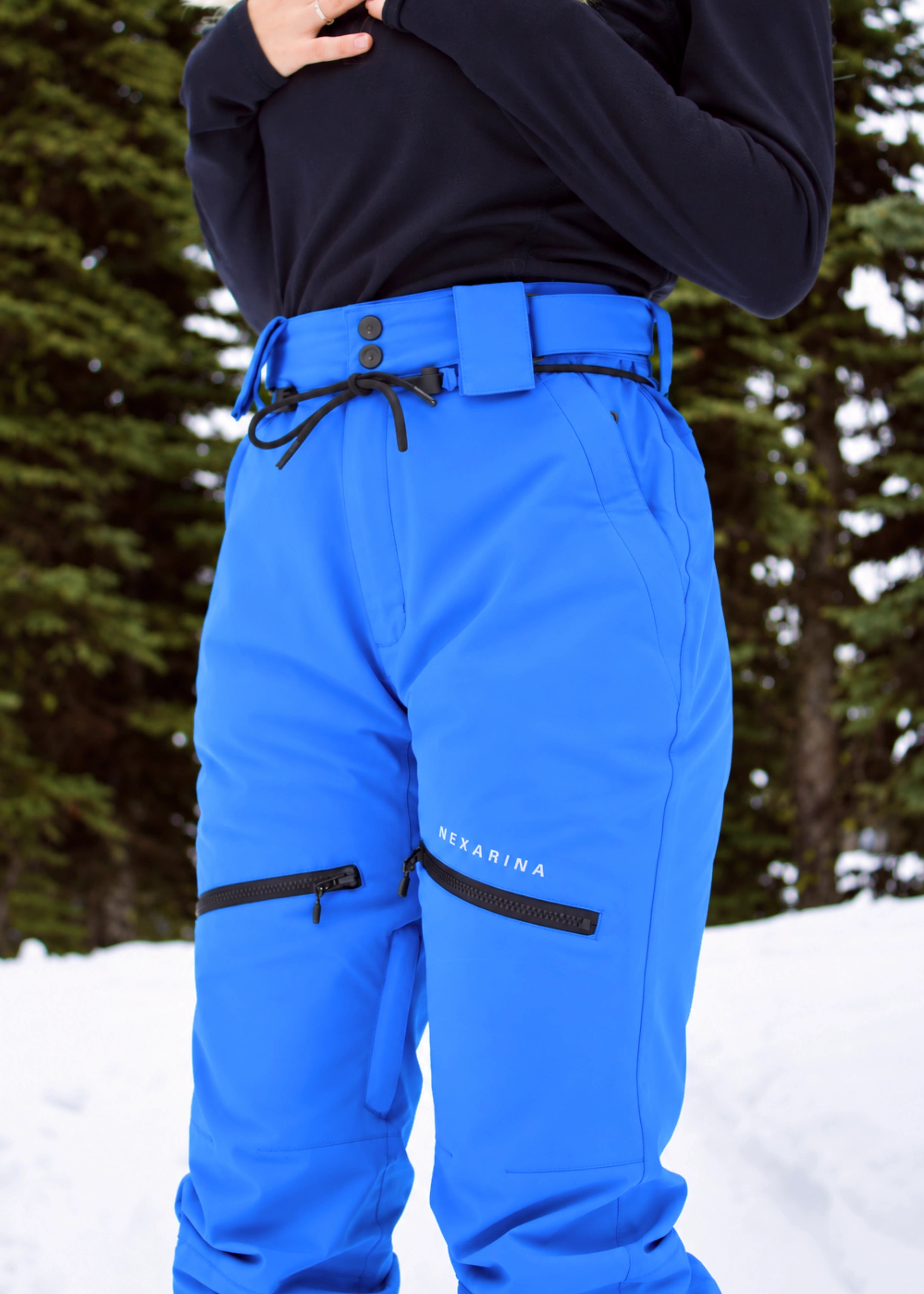 Close-up of Nexarina Avani Arctic Blue snow pants featuring the adjustable waist belt, zippered thigh pockets and Nexarina logo.