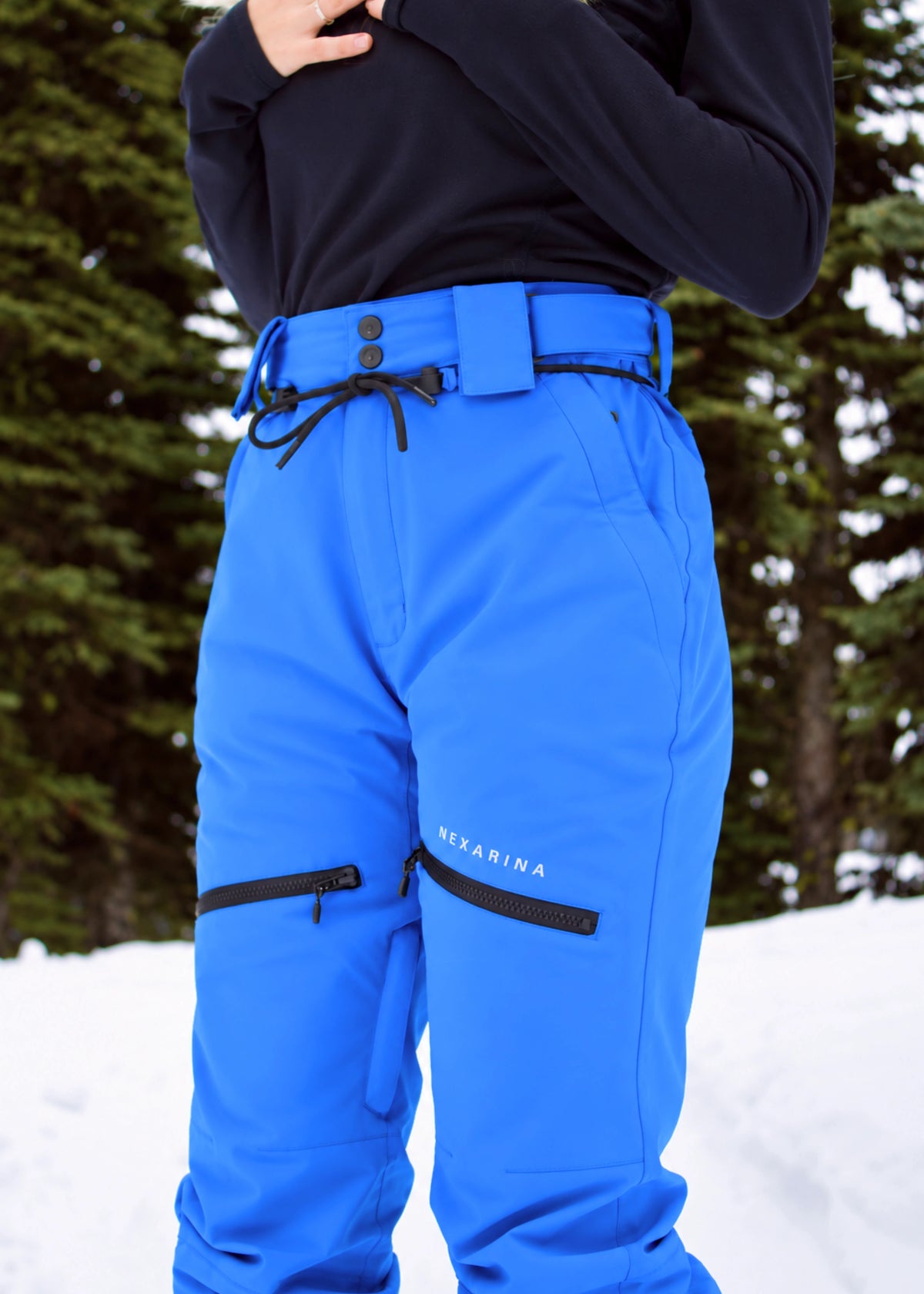 Close-up of Nexarina Avani Arctic Blue snow pants featuring the adjustable waist belt, zippered thigh pockets and Nexarina logo.