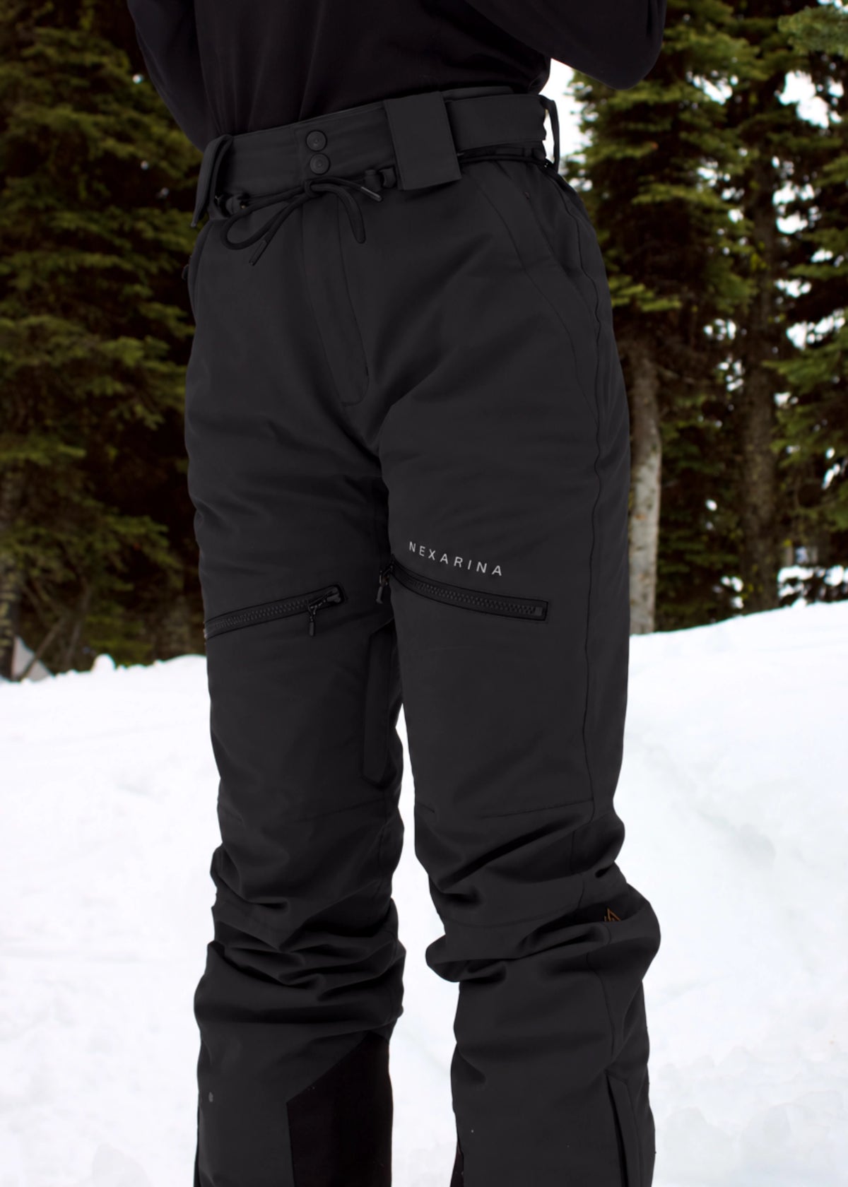 Close-up of Nexarina Avani Classic Black snow pants featuring zippered thigh pockets, adjustable waistband and Nexarina branding.