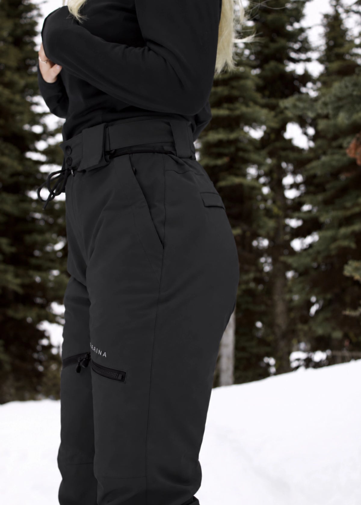 Side view of Nexarina Avani Classic Black women's insulated snow pants, showing the adjustable waistband, contoured hip fit, zippered thigh pocket and rear pocket detail.