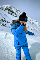  A snowboarder wears blue Avani snow pants, designed for movement, warmth, and protection in winter conditions.