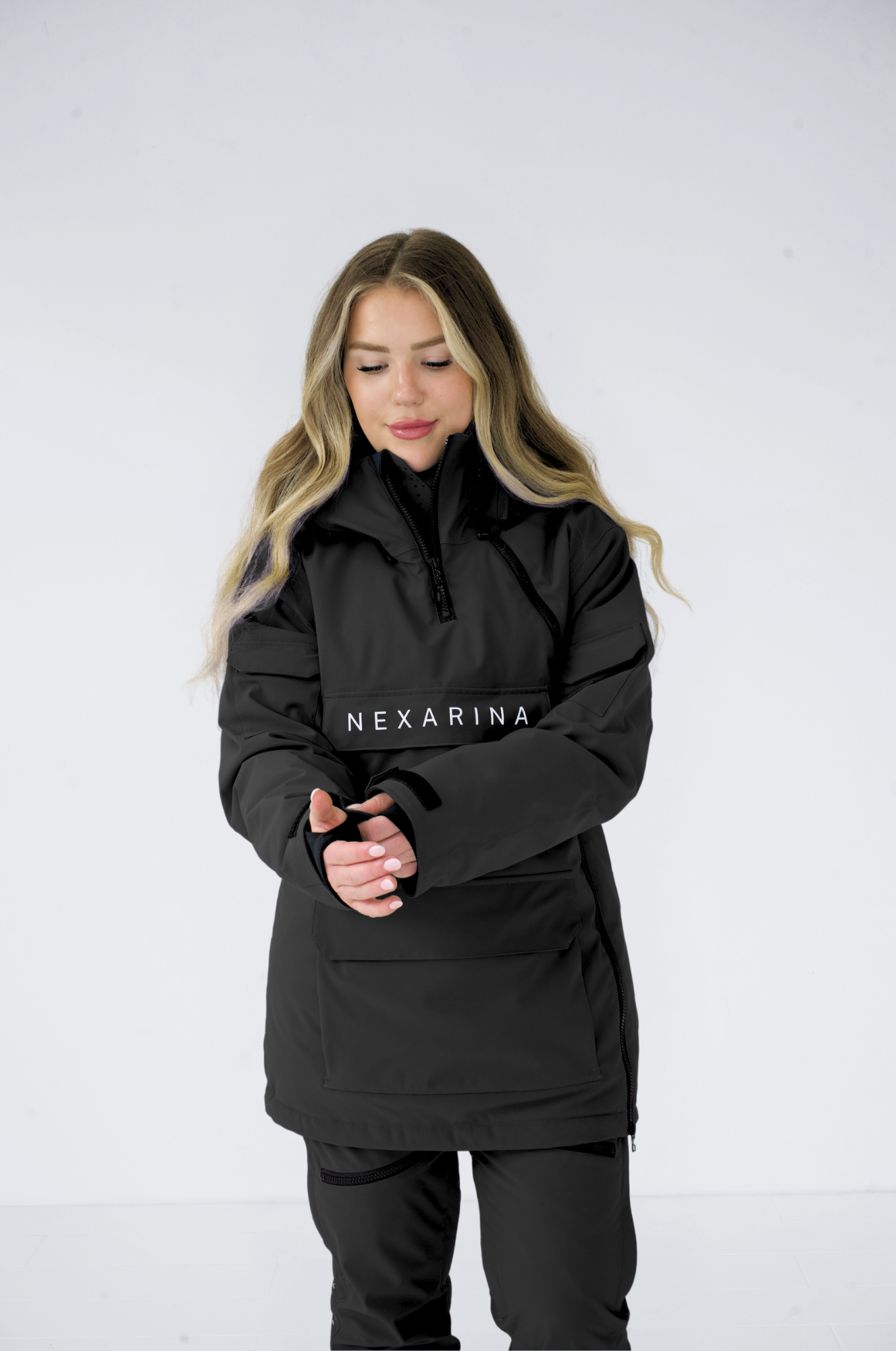 Woman adjusting hood of black Nexarina jacket, front view, standing against a white background.