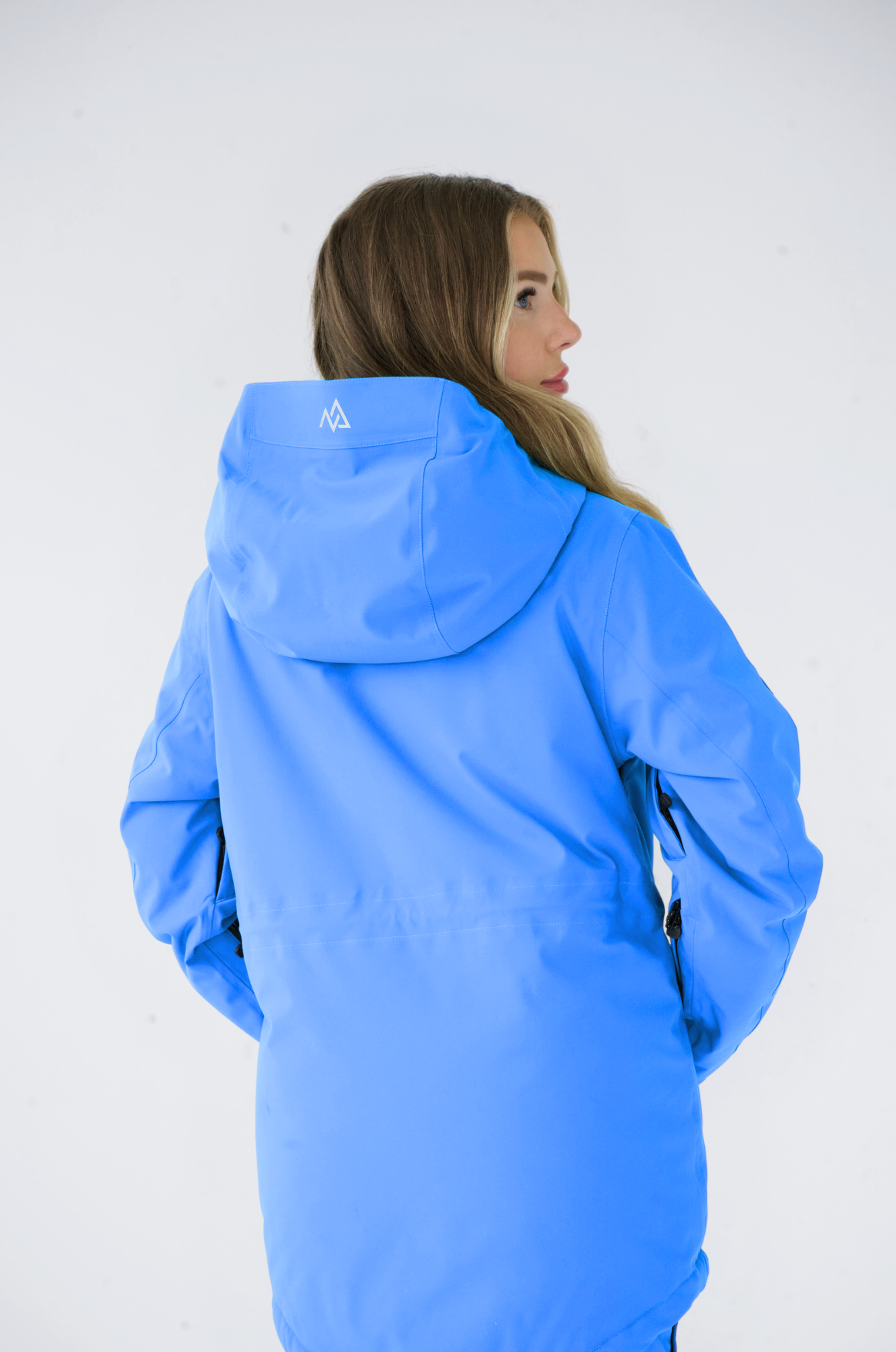 Back view of a woman in a vibrant blue Nexarina snowboard jacket, focusing on the detailed seams and hood