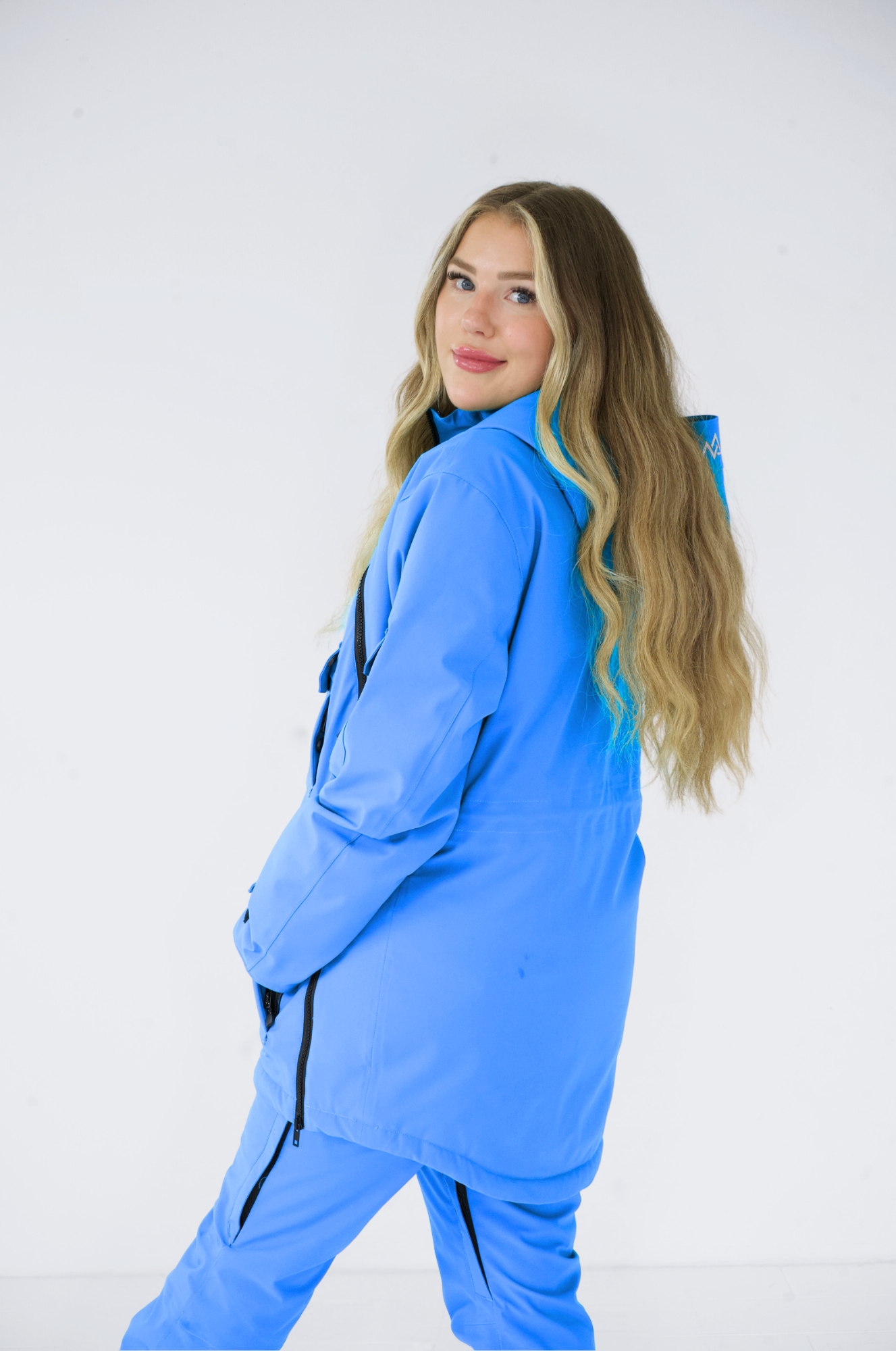 Woman standing sideways in a complete Nexarina blue snowboarding outfit, showcasing the fit and style of the jacket and pants.