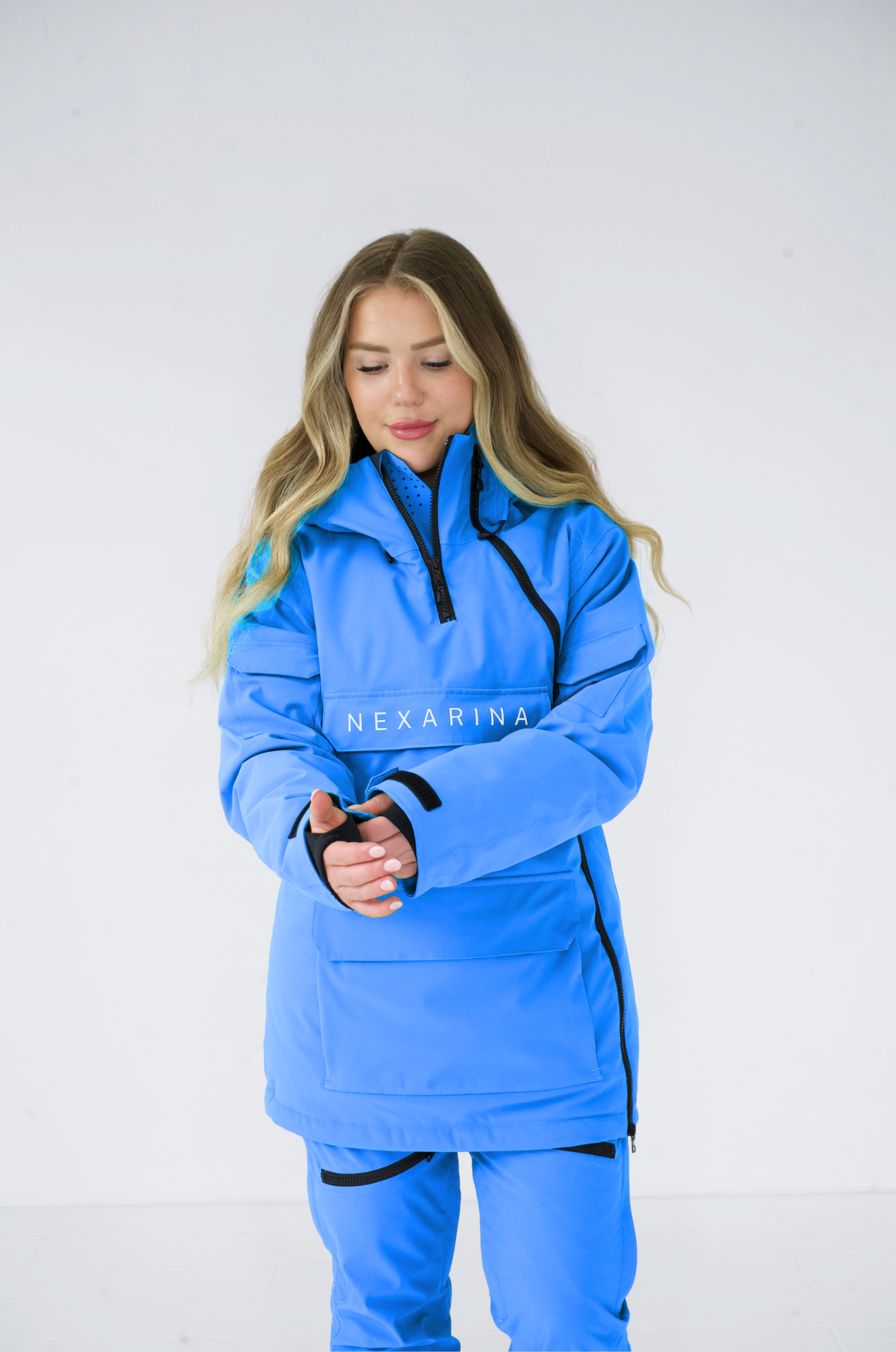 Close-up of a woman adjusting the sleeve of her Nexarina blue snowboarding jacket, highlighting the practical features.