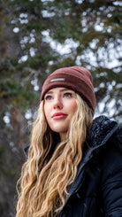 Close-up of a young woman in a Nexarina Coco brown beanie, snow gently falling around her.