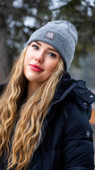 Fashionable winter look featuring a Nexarina Emery Beanie on a woman standing in a snow-covered landscape.