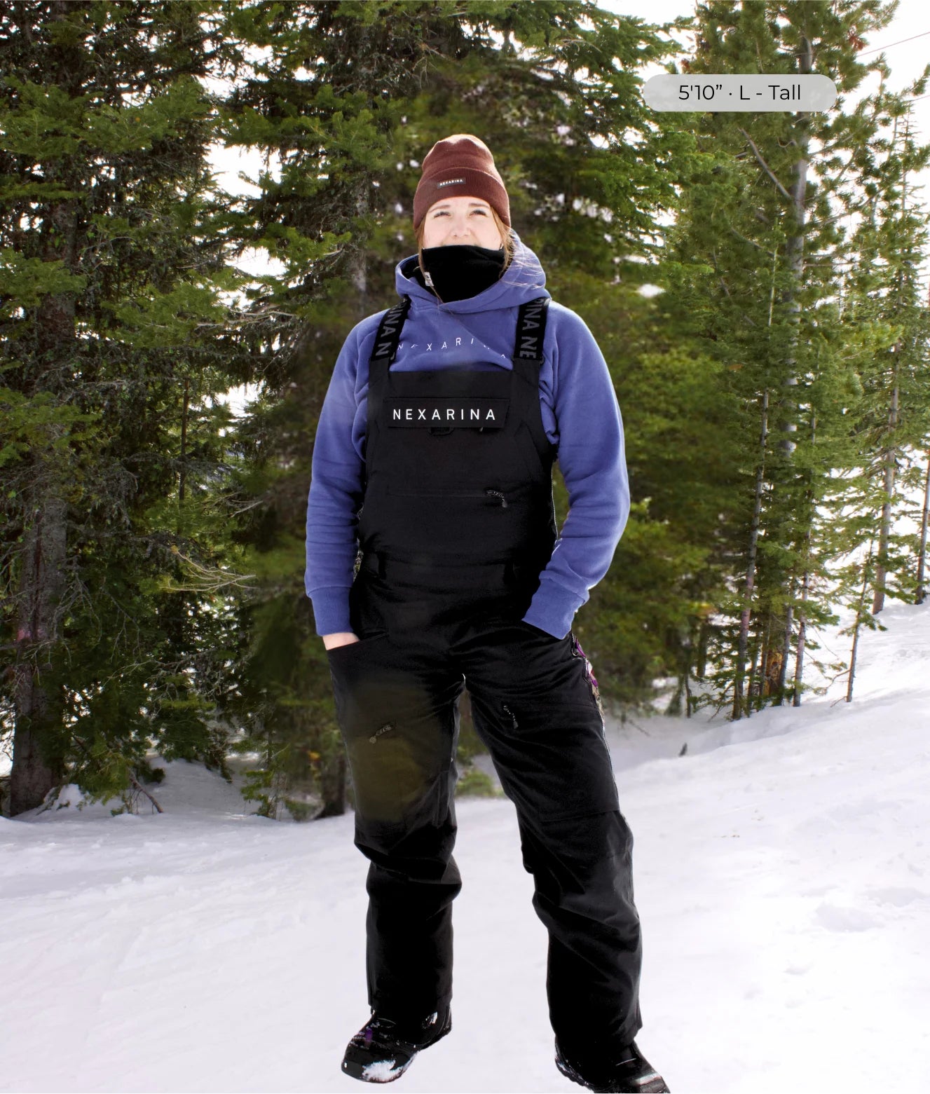 Tall women wearing a blue hoodie and black outerwear bib with 'Nexarina' branding in a snowy forest setting.