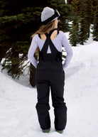 Back view of woman wearing Nexarina Everette Classic Black insulated snow bibs with crossed shoulder straps and stretch back panel.