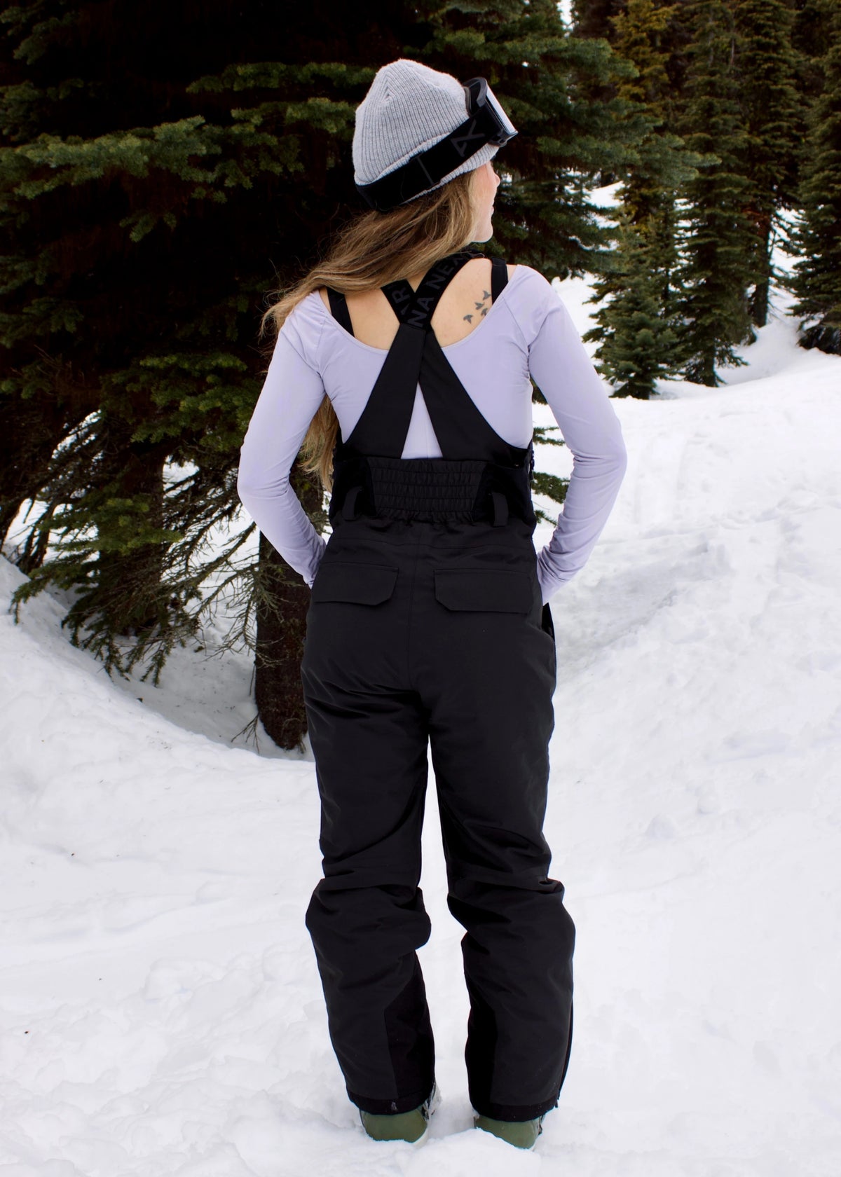 Back view of woman wearing Nexarina Everette Classic Black insulated snow bibs with crossed shoulder straps and stretch back panel.