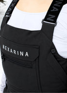Close-up of Nexarina Everette Classic Black snow bibs showing the zippered chest pocket, branded shoulder straps and Nexarina logo.