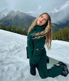 Woman kneeling snow in Nexarina Everette Bib in emerald green, showing full snowboarding outfit.