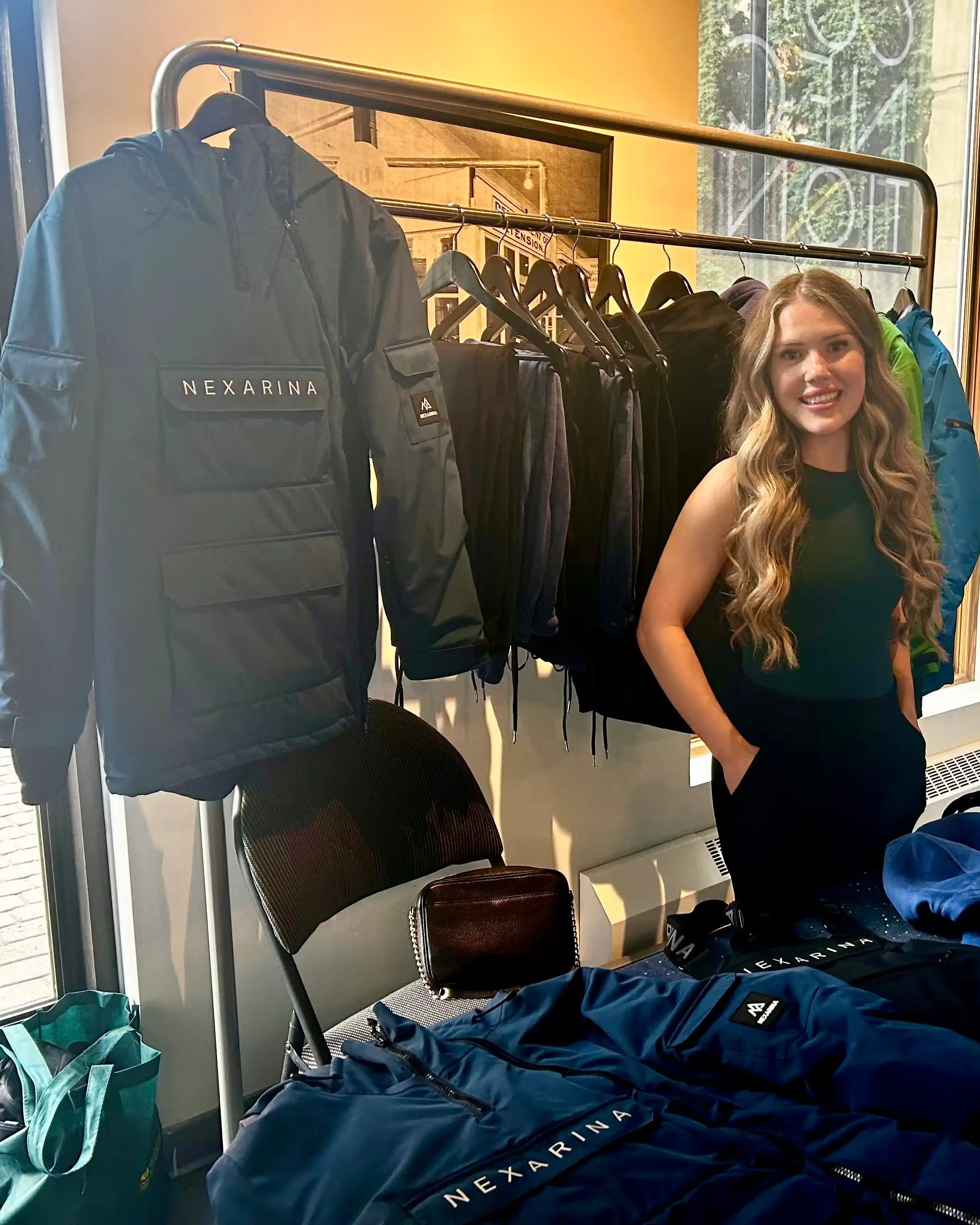 Woman standing in front of a display of jackets with 'Nexarine' branding, in an indoor setting.