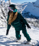 Woman snowboarding in Nexarina Indy snow jacket in emerald green, riding downhill