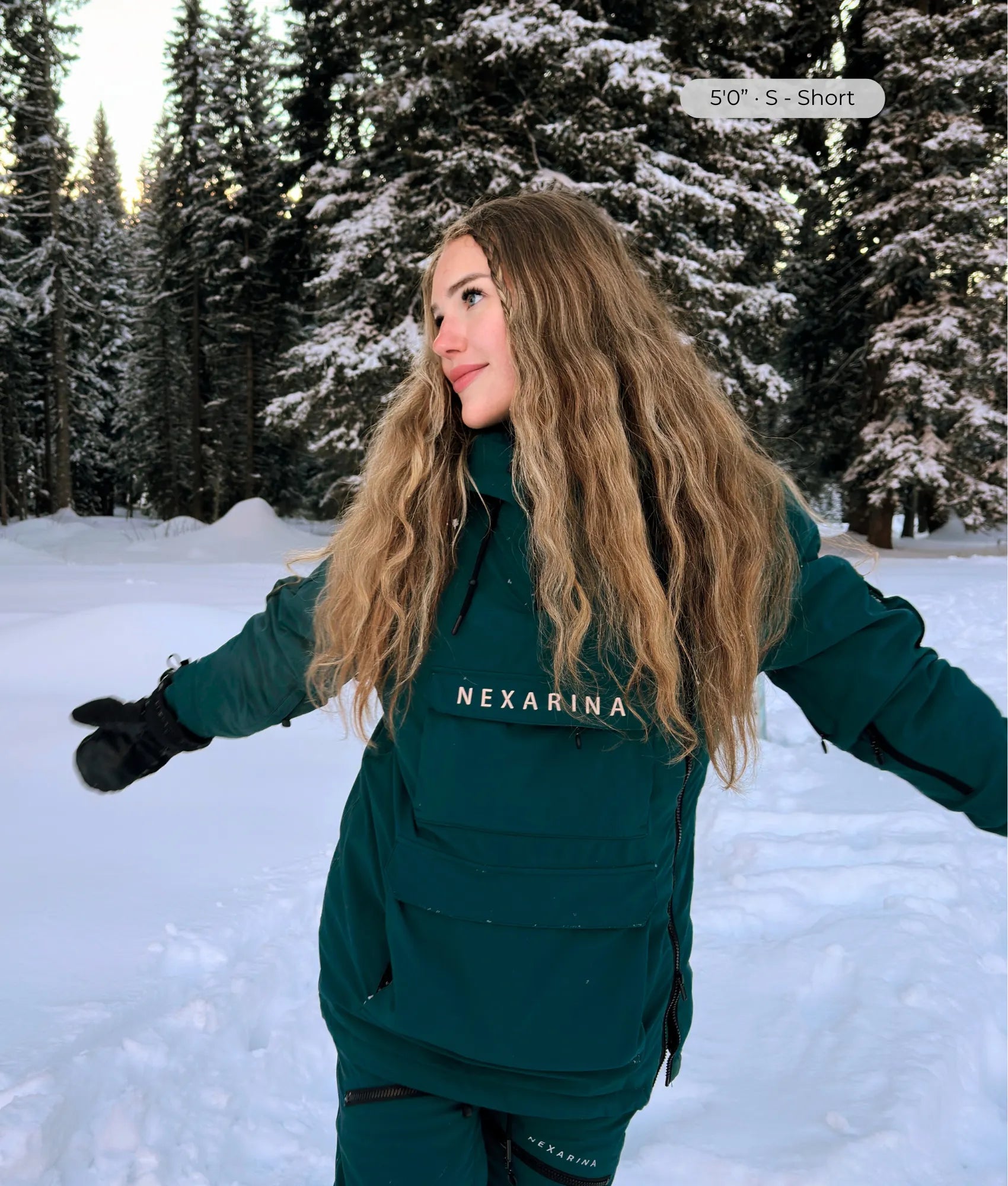 Woman wearing Nexarina Indy emerald green snow jacket, arms out in snowy forest