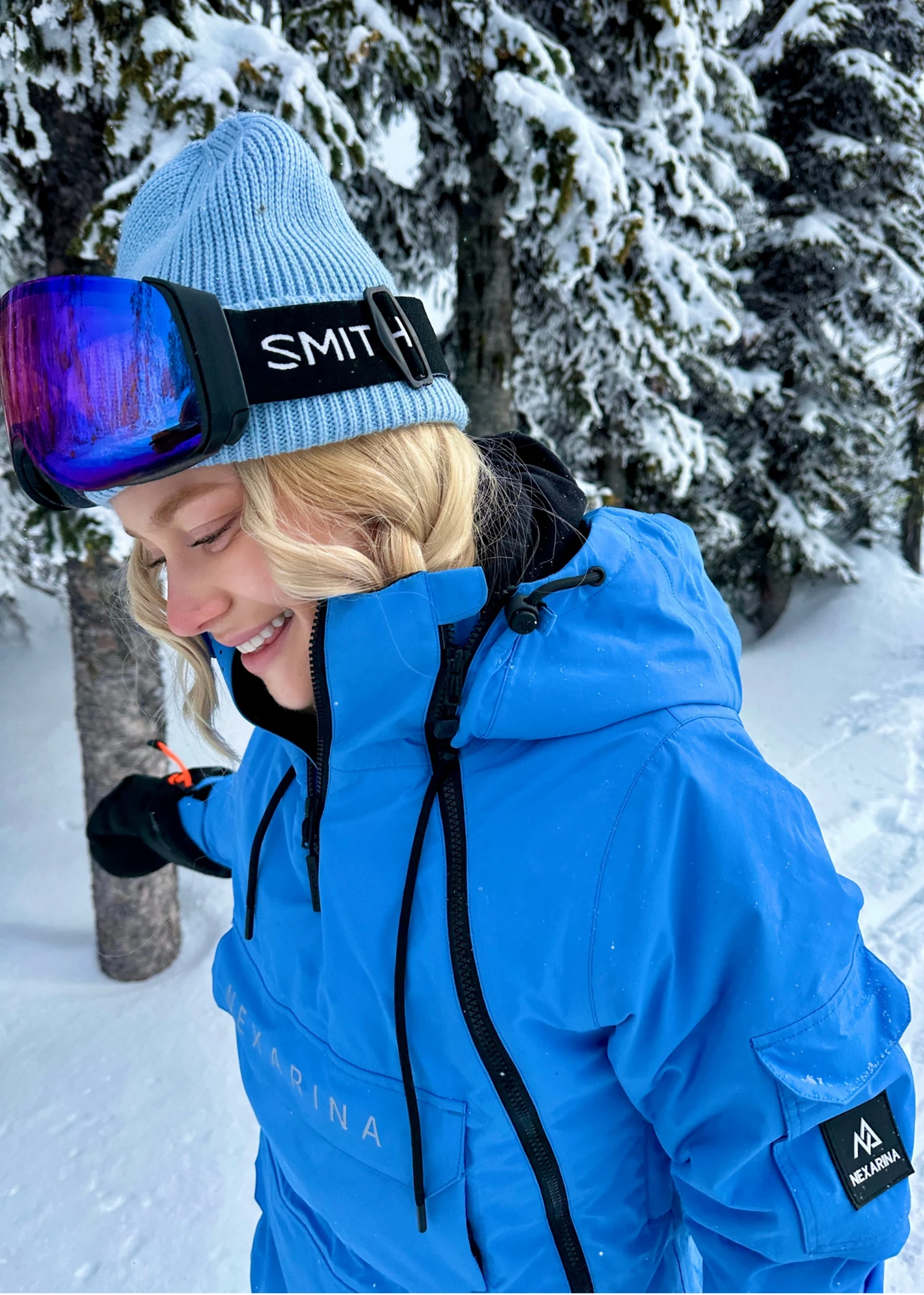 Person wearing a blue jacket and blue beanie with goggles on a snowy background