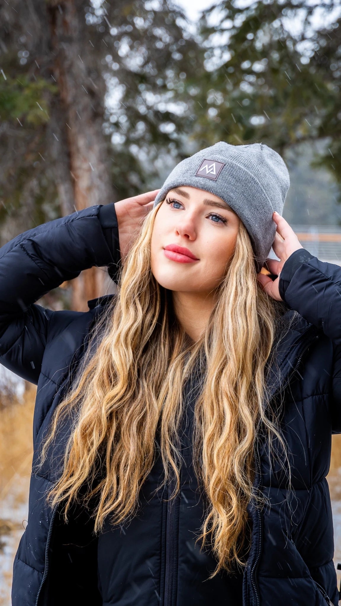 Profile view of a young woman in a grey beanie by Nexarina, gazing into the distance, amidst falling snow.