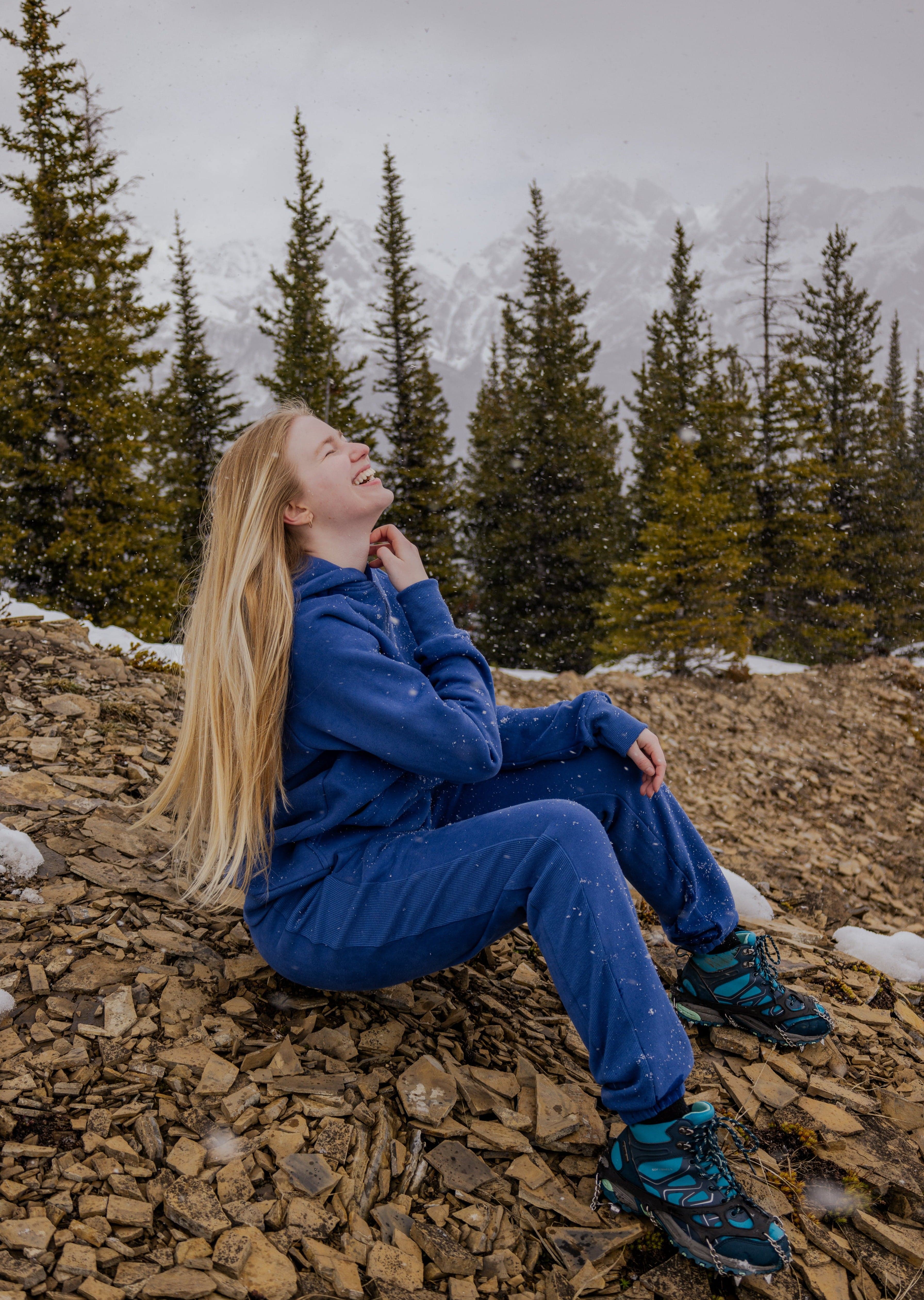 Woman in Nexarina Hoodie laughing while sitting on a snowy mountain.