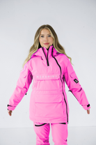 Front view of a woman wearing a pink Nexarina snowboard jacket, looking directly at the camera, against a white backdrop.